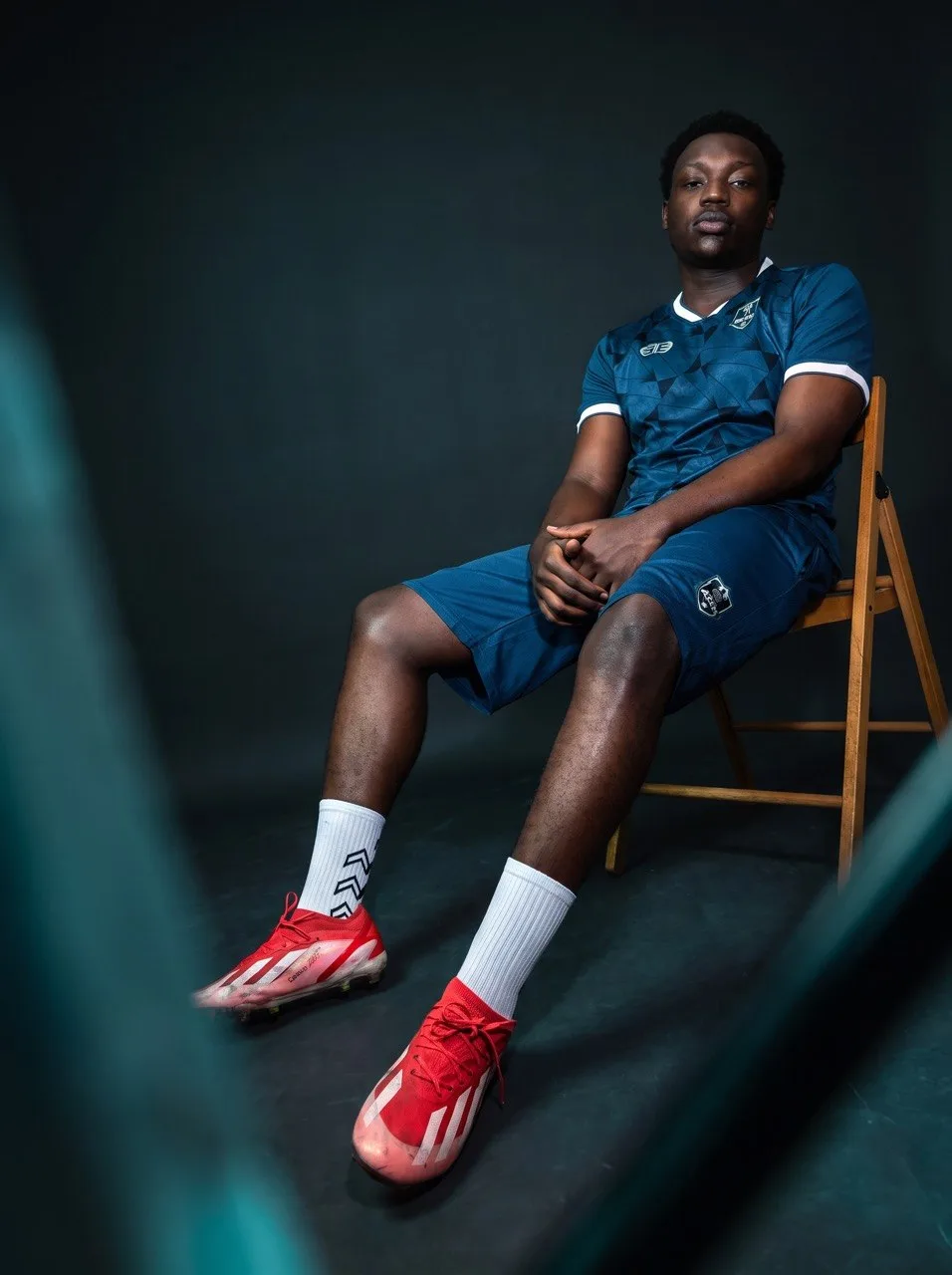 An Aces FC player seated in the club's blue home kit, studio portrait.